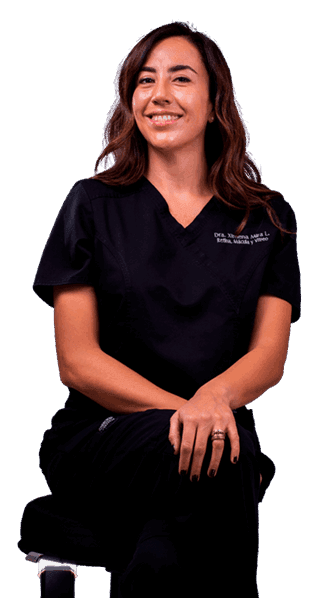 Retrato profesional de la Dra Ximena Mira con uniforme clínico, sentada y sonriendo, en contexto médico.